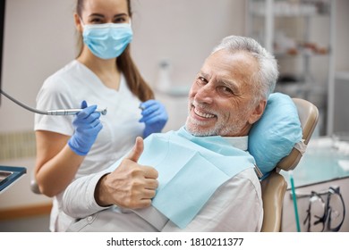 Joyful Senior Citizen Sitting In A Dental Chair Showing Thumbs Up While Being Treated By A Female Dentist