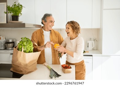 Joyful senior couple arriving from supermarket with grocery bag and unpacking in kitchen, elderly spouses enjoying life, spending time helping each other - Powered by Shutterstock