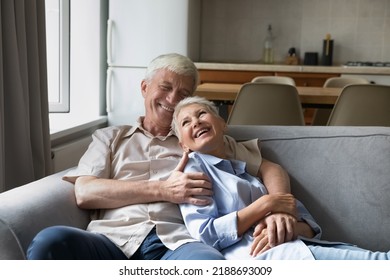 Joyful Senior Couple Enjoy Rest And Conversation Sit On Cozy Sofa, Having Warm Harmonic Relationship, Happy Marriage And Endless Love. Elderly Homeowner Family Spend Leisure At Modern Own Home