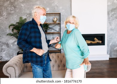Joyful Senior Couple With A Medical Mask On Their Faces Has Fun Together At Home During Pandemic, Quarantine. A Mature Man And Senior Woman Wearing Protective Masks Dancing In The Living Room
