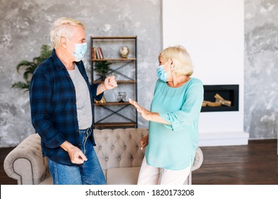 Joyful Senior Couple With A Medical Mask On Their Faces Has Fun Together At Home During Pandemic, Quarantine. A Mature Man And Senior Woman Wearing Protective Masks Dancing In The Living Room