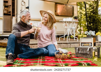 Joyful senior couple spouses travelers husband and wife toasting with glasses of champagne celebrating sitting on the blanket in the caravan porch, on a trip together in camper van - Powered by Shutterstock