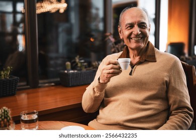 Joyful senior man in warm clothing drinking coffee and relaxing in the city cafe while sitting by the window at evening. - Powered by Shutterstock