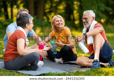 Joyful senior yoga enthusiasts enjoying friendly chat while sitting on mats outdoors, happy elderly people holding water bottles, older men and women relaxing after refreshing session in summer park
