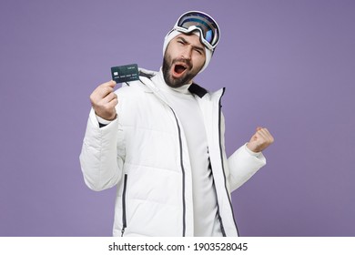 Joyful Skier Man In Warm White Windbreaker Jacket Ski Goggles Mask Hold Credit Bank Card Doing Winner Gesture Spend Weekend In Mountains Isolated On Purple Background. People Lifestyle Hobby Concept