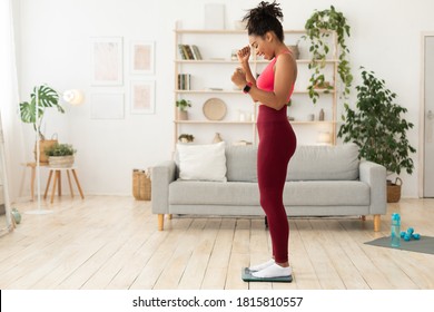 Joyful Skinny Black Woman Weighing Herself After Successful Dieting And Weight Loss Standing On Weight-Scales At Home. Slimming, Caring For Body Concept. Blank Space For Text