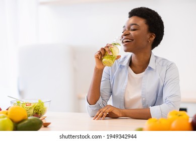 Joyful Slim Black Woman Drinking Infused Water For Healthy Hydration And Refreshment Posing With Bottle In Kitchen At Home. Slimming And Weight Loss. Stay Hydrated Concept