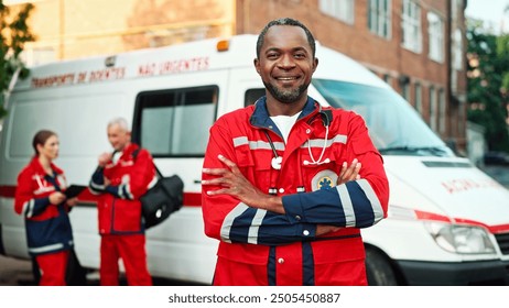 Joyful smiling African American male doctor in red medical uniform looking at camera standing outdoor near ambulance vehicle. Paramedics with tablet device on background, first aid, healthcare concept - Powered by Shutterstock