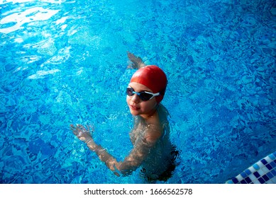 Joyful smiling boy swimmer in a cap and Goggles learns professional swimming in the swimming pool in gym close up - Powered by Shutterstock