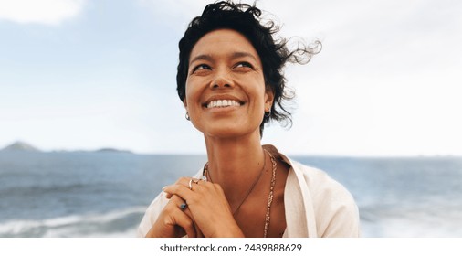 Joyful smiling woman with wavy hair and bohemian jewelry posing in a close-up portrait at the seaside on a windy day. - Powered by Shutterstock