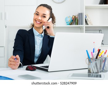 joyful smiling young woman having negotiations by phone in office