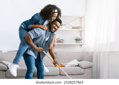 Joyful Spring-Cleaning. Playful African American Couple Fooling Together During Tidying Flat, Woman Piggybacking Her Boyfriend While He Mopping Floor - Powered by Shutterstock