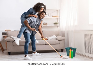 Joyful Spring-Cleaning. Playful African American Couple Fooling Together During Tidying Flat, Woman Piggybacking Her Boyfriend While He Mopping Floor - Powered by Shutterstock