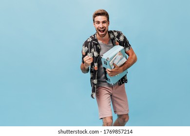 Joyful stylish young man with cool hairstyle and beard in modern summer shirt and beige shorts holding blue suitcase and rejoices.. - Shutterstock ID 1769857214