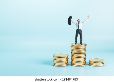 Joyful and successful businessman in a suit standing on a pile of coins at abstract blue background. Earning money concept.