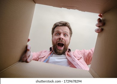 Joyful, surprised Caucasian man unpacks a delivered box with a parcel or a gift. Unboxing inside view.