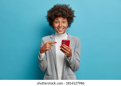 Joyful surprised woman employee opens calendar on mobile phone for planning appointment, points at smartphone display and wears formal outfit. Female office worker happy to check balance on salary day