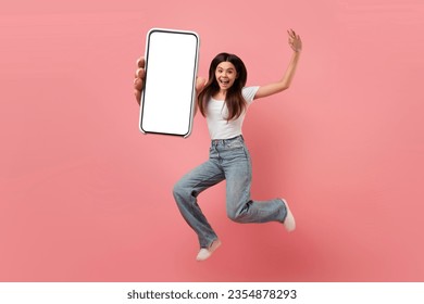 Joyful teen girl jumping in air with big blank smartphone in hand, carefree female teenager demonstrating empty mobile phone, young woman having fun on pink studio background, collage, mockup - Shutterstock ID 2354878293