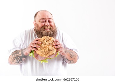 Joyful thick guy eating big bun with meat