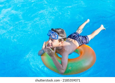 A Joyful White Eastern European 9-year-old Boy On A Rainbow Inflatable Circle With Swimming Glasses Enjoys Life