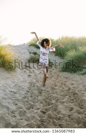 Joyful woman dancing and having fun on vacation at the beach. Spring or summer outdoor relaxing leisure. Afro hair young black female. Asturias, Spain.