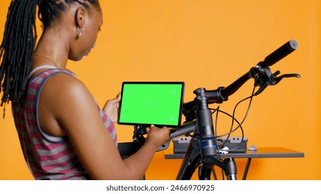 Joyful woman following tutorial videos on mockup tablet, learning to mend broken bike. Smiling cycling hobbyist having fun repairing bicycle, following online guide on green screen device, camera B - Powered by Shutterstock