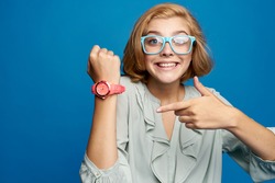 Joyful Woman In Glasses Shows A Clock On A Blue Background Portrait                               