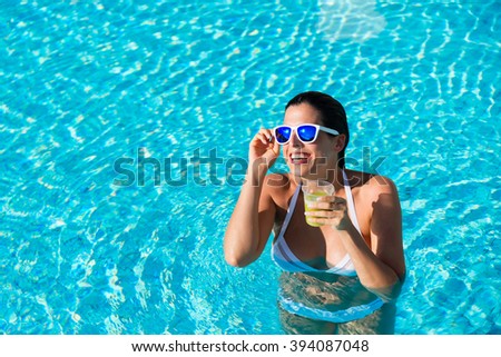Joyful woman having fun bathing in hotel resort spa pool and drinking cocktail on summer vacation.