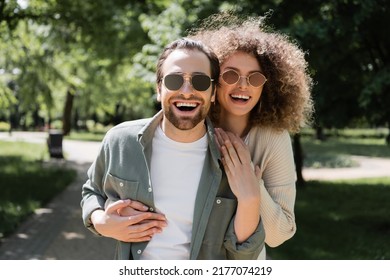 Joyful Woman Hugging Happy Man In Stylish Sunglasses In Park