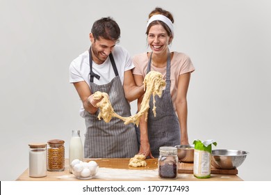 Joyful Woman And Man Couple Wear Aprons, Make Homemade Pasta Of Dough, Have Fun At Kitchen, Work As Friendly Team, Prepare Pizza At Home, Isolated On White Backgrpund. Family Cooking Concept