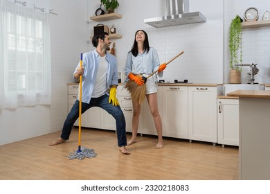 Joyful woman singing songs and dancing with closed eyes while cleaning kitchen at home. Happy young couple having fun while doing cleaning the floor at home and pretend to sing song with mop. - Powered by Shutterstock