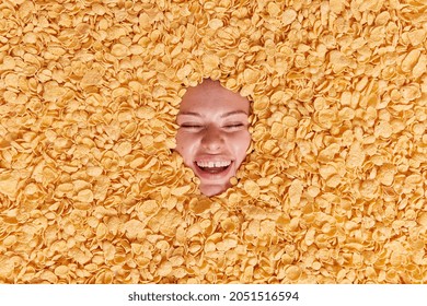 Joyful Woman Smiles Happily Keeps Eyes Closed Being In Good Mood Buried In Cornflakes Feels Very Happy Has Healthy Breakfast Eats Low Calorie Food Keeps To Diet. Weight Losss And Balanced Nutrition