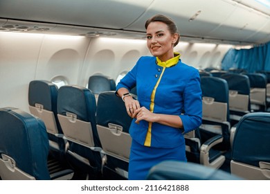 Joyful woman stewardess in airline air hostess uniform looking at camera and smiling while resting hand on passenger seat