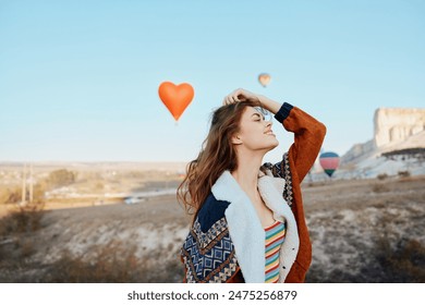 joyful woman surrounded by colorful balloons with heart shaped balloon floating in front of majestic mountain - Powered by Shutterstock