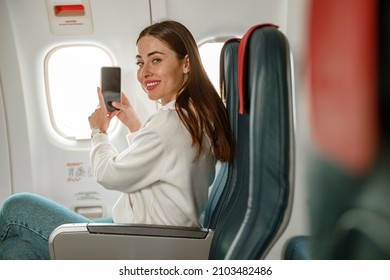 Joyful woman taking photo with smartphone in airplane