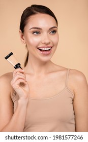 Joyful Woman With Tube Of Concealer Looking Away Isolated On Beige