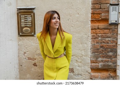 Joyful Woman In Yellow Clothes Looking Away Near Wall On Venetian Street