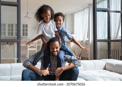 Joyful Young African American Dad Playing With Kids, Piggybacking Two Siblings On Neck. Happy Excited Kids Riding Together On Strong Daddy Shoulders, Playing Active Games, Having Fun