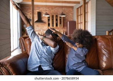 Joyful Young African American Father Making Trendy Dub Move With Happy Little Kid Daughter, Having Fun Resting Together On Comfortable Sofa, Cheerful Multigenerational Family Entertaining Indoors.