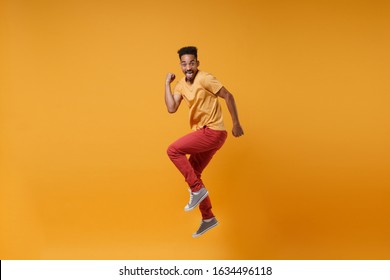 Joyful young african american guy in casual clothes posing isolated on yellow orange wall background studio portrait. People lifestyle concept. Mock up copy space. Jumping clenching fists like winner