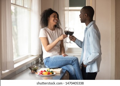 Joyful young african american woman sitting on countertop, holding glass of red wine, cheering with happy mixed race husband. Smiling ethnic family couple celebrating special occasion or meeting. - Powered by Shutterstock