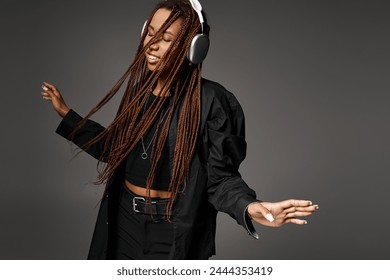 joyful and young African American woman in 20s with headphones dancing to music on grey backdrop - Powered by Shutterstock