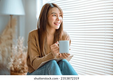 Joyful young asian female enjoying a cup of coffee while sitting on bench at home, Cosy scene, Smiling pretty woman drinking hot tea in autumn winter. - Powered by Shutterstock