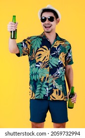 Joyful Young Asian Man With Sunglasses Smiling And Raising A Beer Bottle With Right Hand. Medium Long Shot Studio Portrait On Yellow Background. Cheerful And Happy People In Summer Holidays Concept