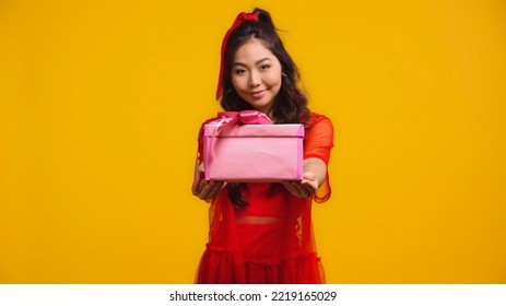 Joyful Young Asian Woman Holding Wrapped Present Isolated On Yellow 