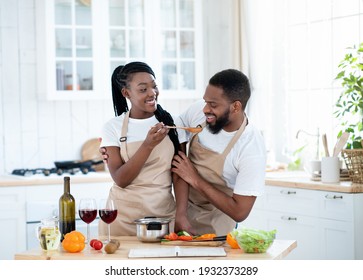 Joyful Young Black Spouses Tasting Food While Cooking Lunch In Kitchen, Happy African American Family Preparing Food At Home And Drinking Wine, Enjoying Spending Time Together, Copy Space - Powered by Shutterstock