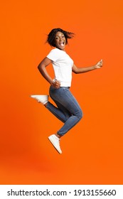 Joyful young black woman posing on orange studio background, full length photo. Emotional african american beautiful lady jumping up and screaming, showing happiness and joy