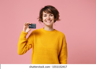 Joyful Young Brunette Woman Girl In Yellow Sweater Posing Isolated On Pastel Pink Wall Background Studio Portait. People Sincere Emotions Lifestyle Concept. Mock Up Copy Space. Hold Credit Bank Card