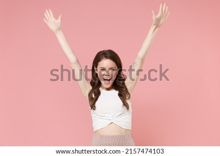 Joyful young brunette woman girl in light casual clothes posing isolated on pastel pink wall background studio portrait. People emotions lifestyle concept. Mock up copy space. Spreading rising hands