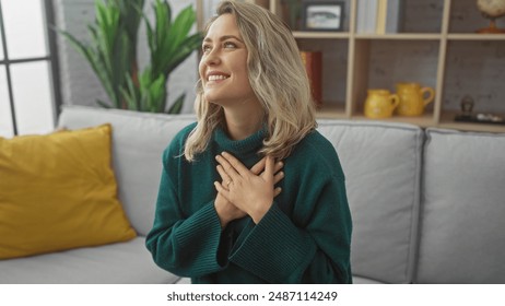 A joyful young caucasian woman places her hands on her heart in a cozy home interior with modern decor. - Powered by Shutterstock